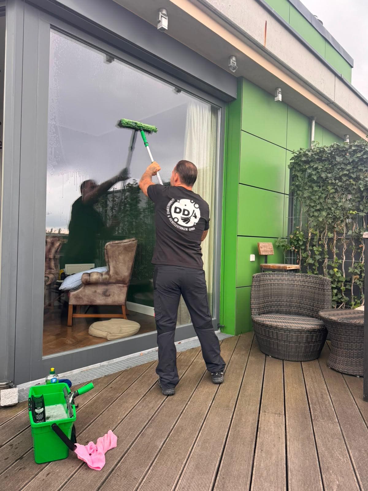 DDA-Mitarbeiter reinigt eine große Glasfront von einer Holzterrasse aus